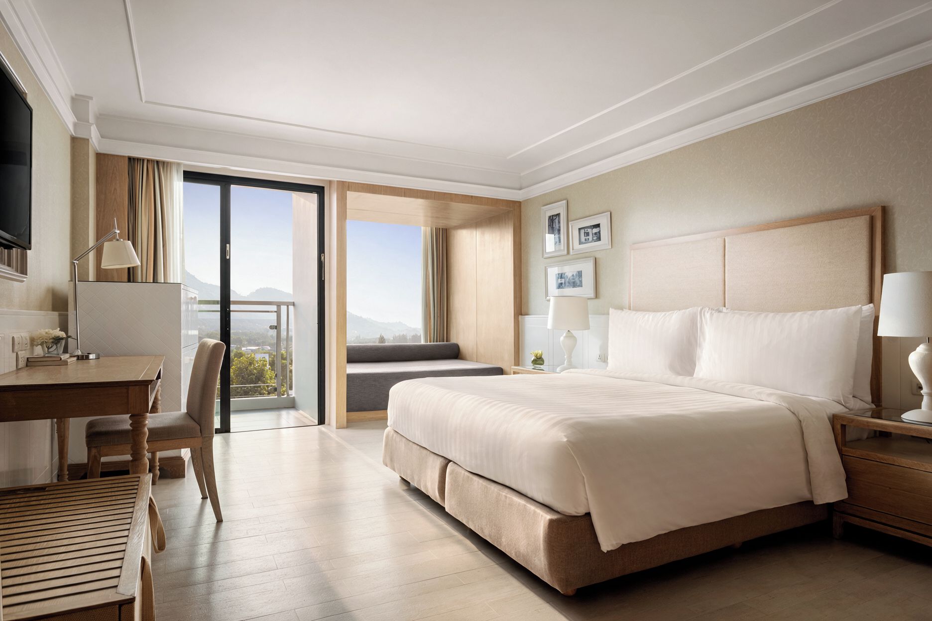 A hotel room with a bed, a desk, a chair, a TV, and a view of the outdoors.