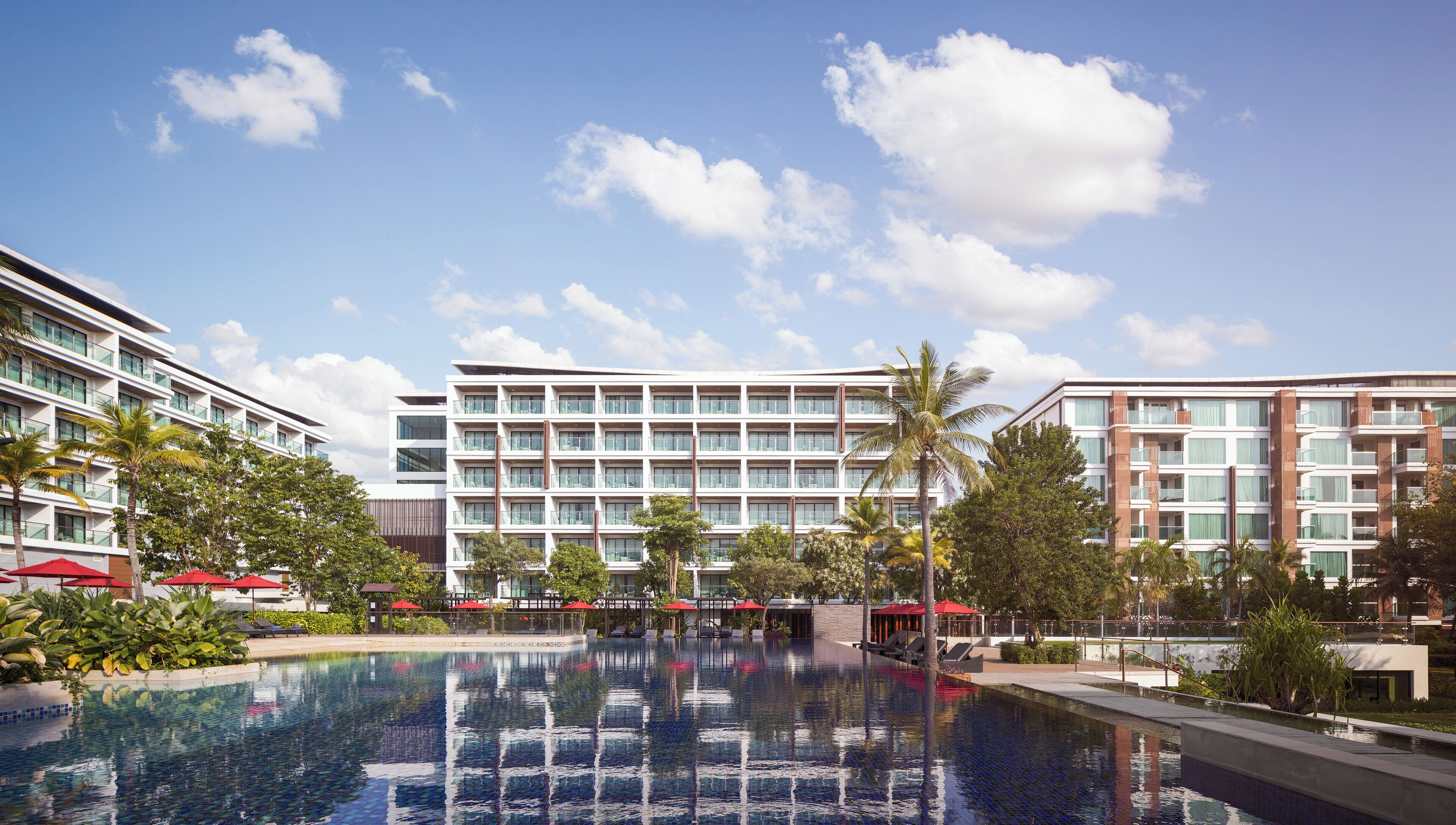 Un hotel moderno con una piscina amplia, varios balcones y exuberante vegetación.