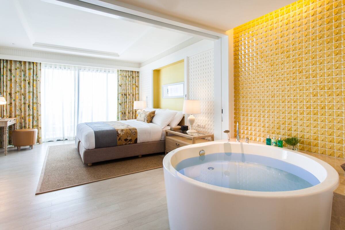Una habitación de hotel con una cama grande, una bañera y una pared amarilla con textura.