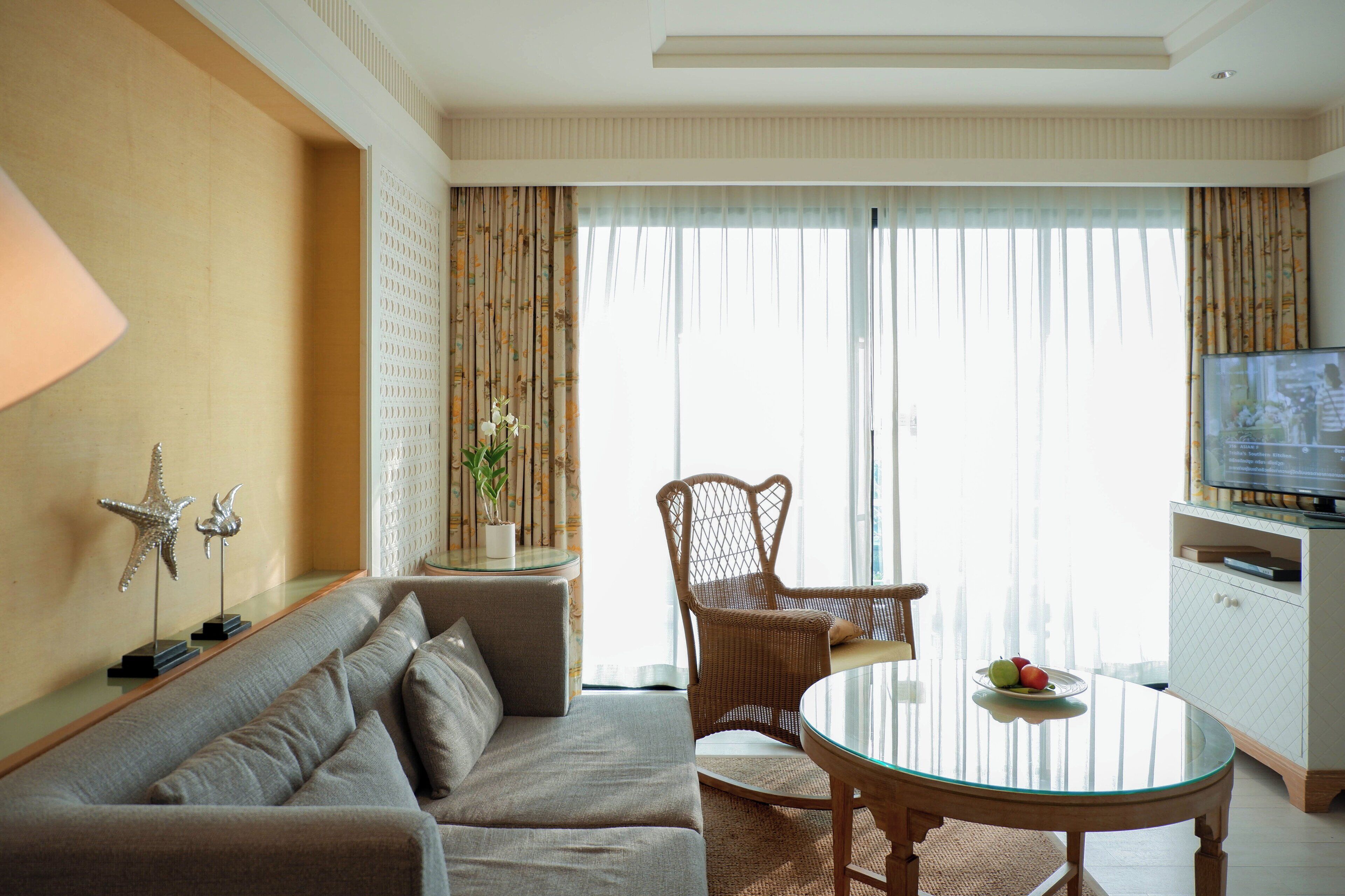A modern living room with a sofa, a glass table, a wicker chair, and a television.