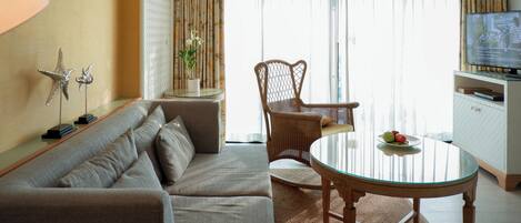 A modern living room with a sofa, a glass table, a wicker chair, and a television.