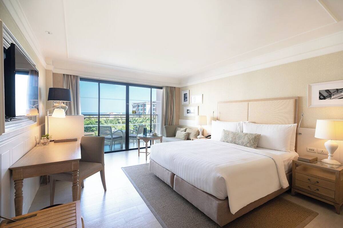 Habitación de hotel con una cama grande, un escritorio, una silla, una mesita y un balcón con vistas.