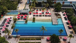 Vista aérea de un hotel con una gran piscina rodeada de sillones de playa y sombrillas rojas.