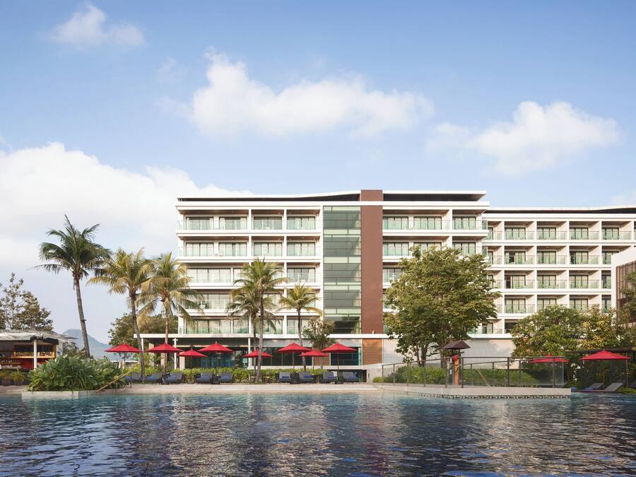 A hotel with a pool, multiple floors, and red umbrellas.