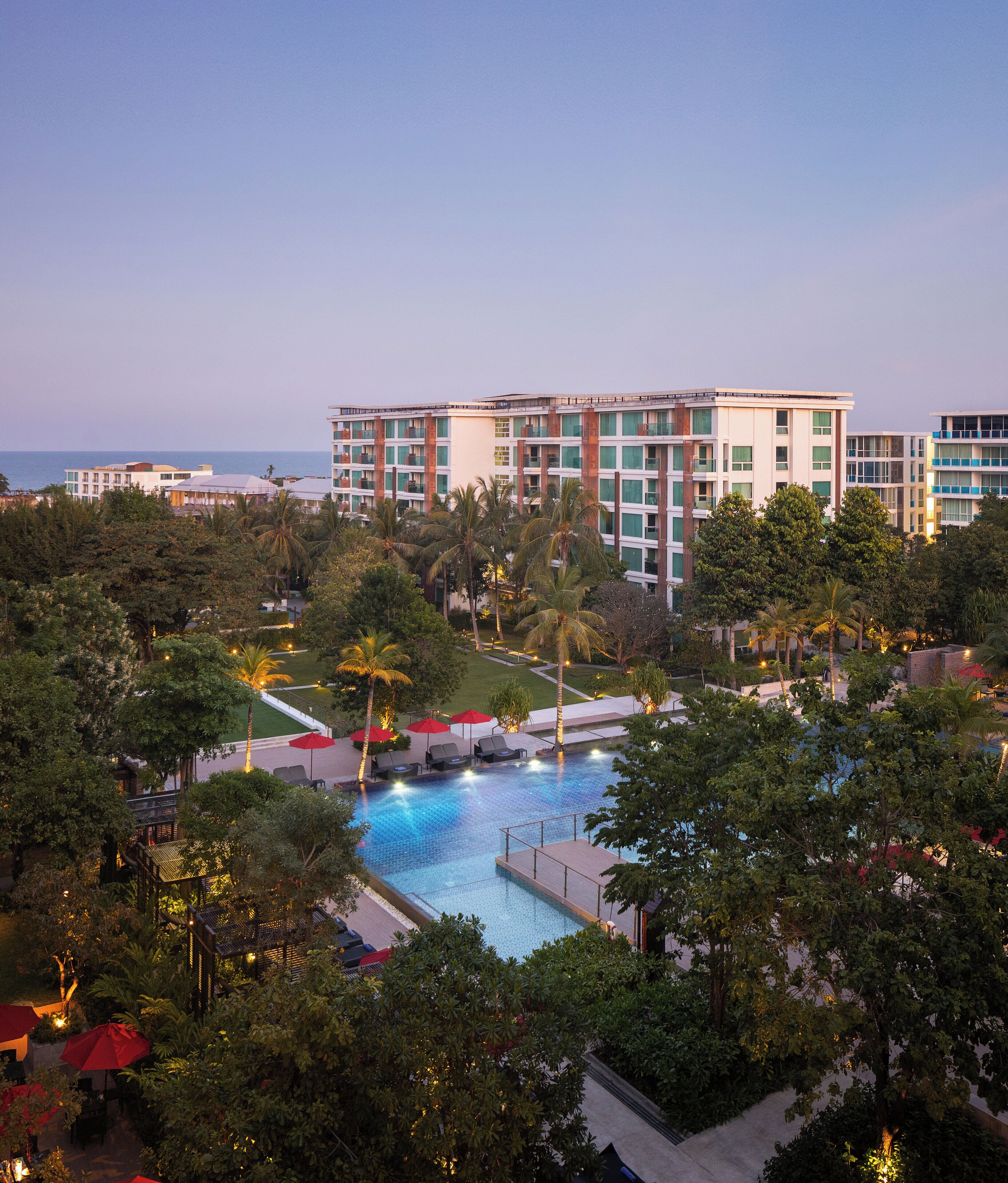 Un hotel con piscina rodeado de palmeras y vistas al mar.