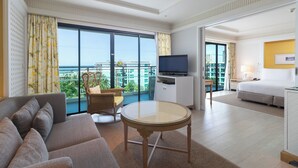 Habitación de hotel con sofá, una pequeña mesa redonda, televisión y balcón con vista a la ciudad.