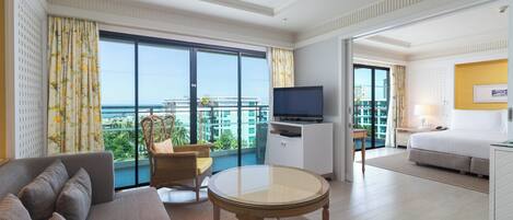 Une chambre d’hôtel avec un canapé, une petite table ronde, une télévision et un balcon offrant une vue sur la ville.