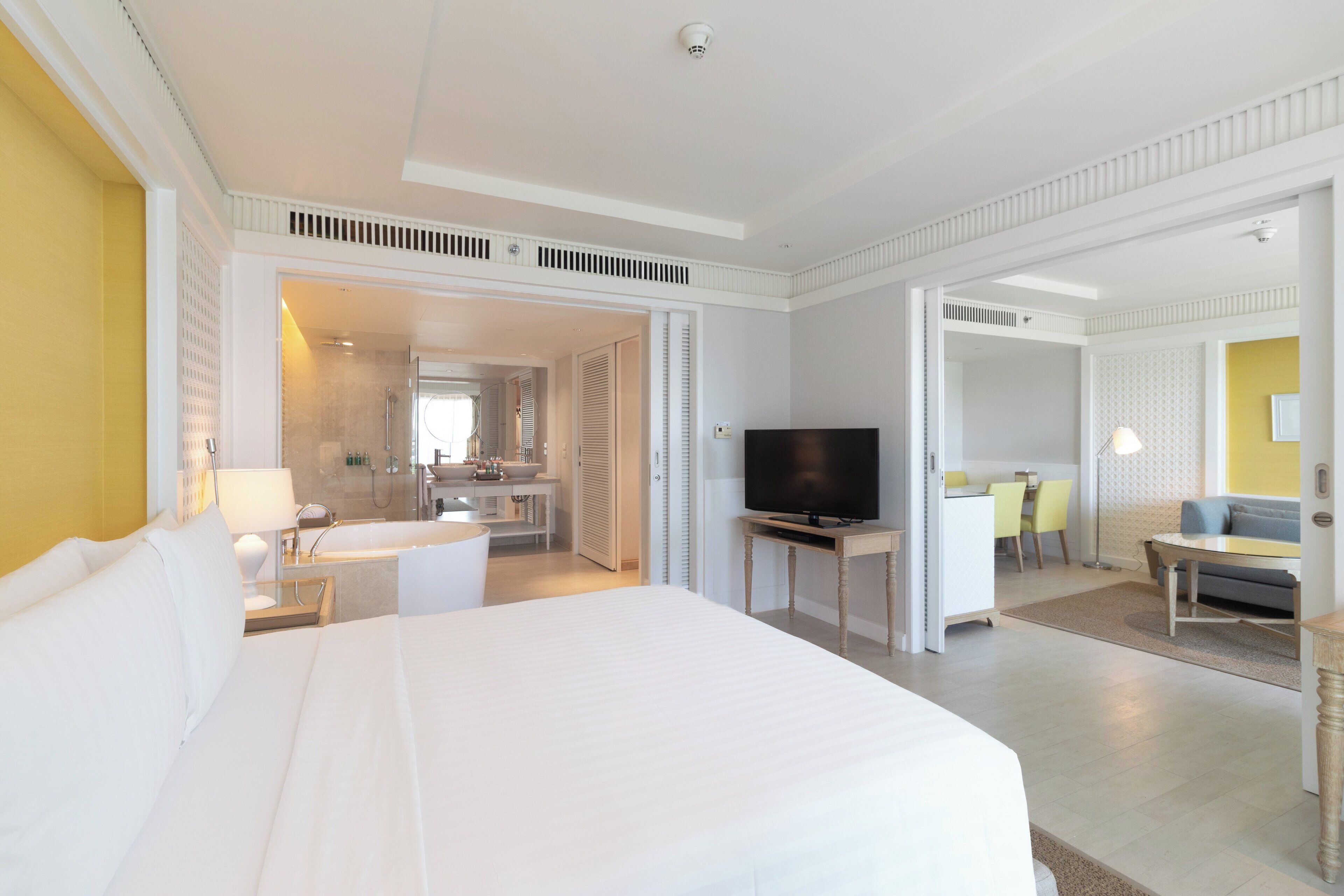 Habitación de hotel con una cama grande, televisor, baño con ducha y zona de comedor con mesa y sillas.