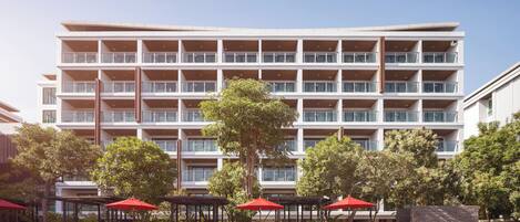 A hotel with a large pool area, multiple balconies, and outdoor seating with umbrellas.