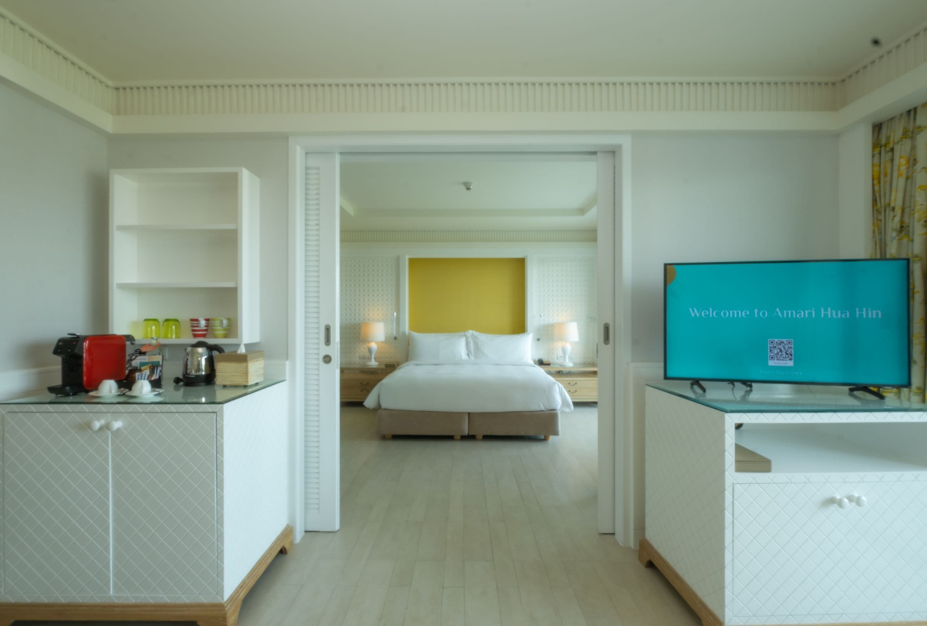 A hotel room with a bed, a TV, a desk with a coffee maker, and a minibar.