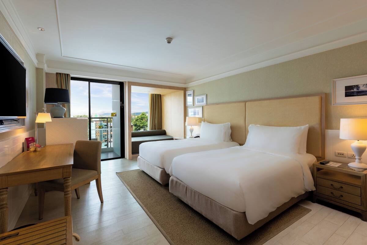 Una habitación de hotel con dos camas, un escritorio, una silla, un televisor y un balcón.