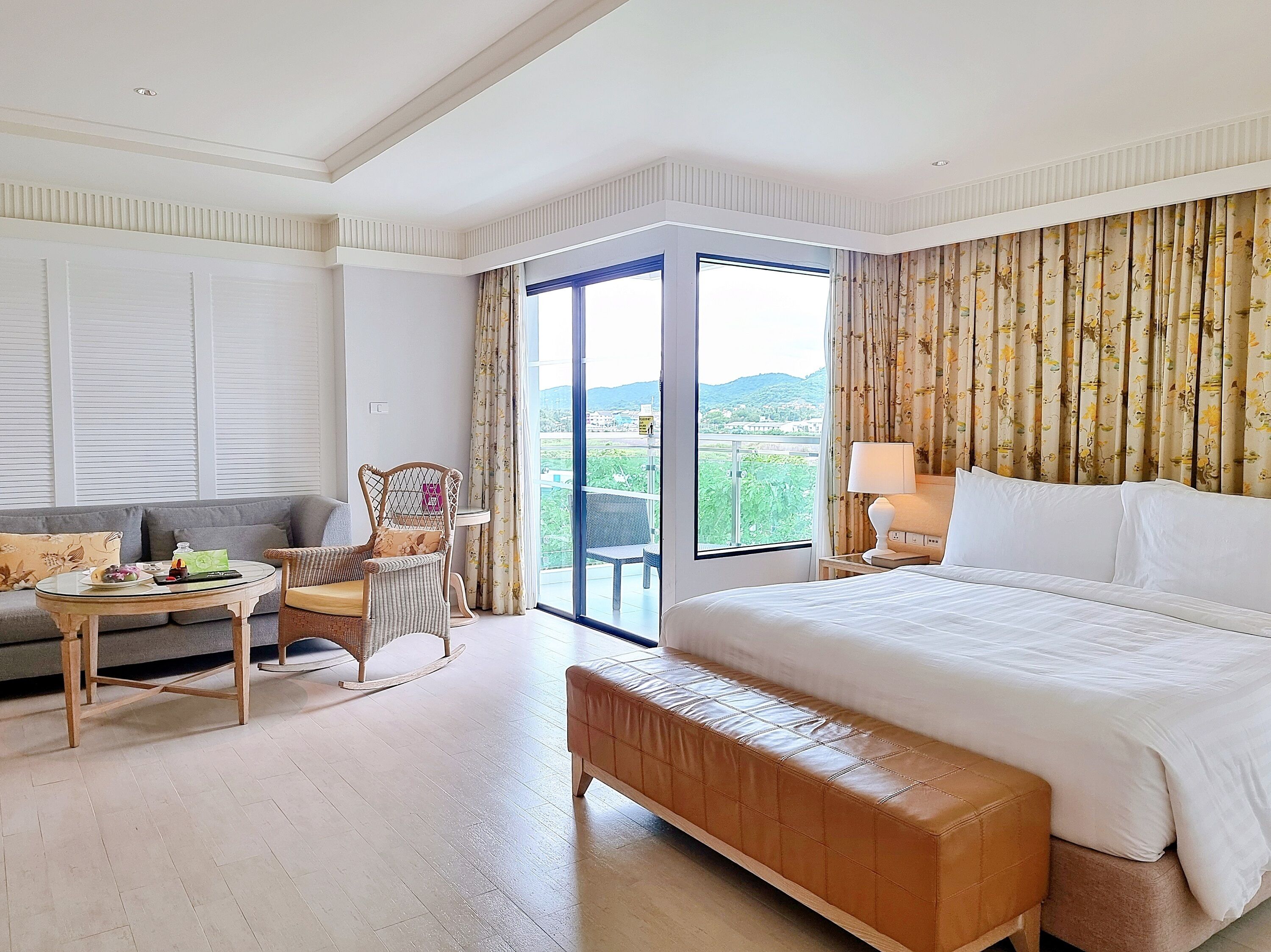 A hotel room with a bed, a sofa, a rocking chair, a small table, and a view of the outdoors.