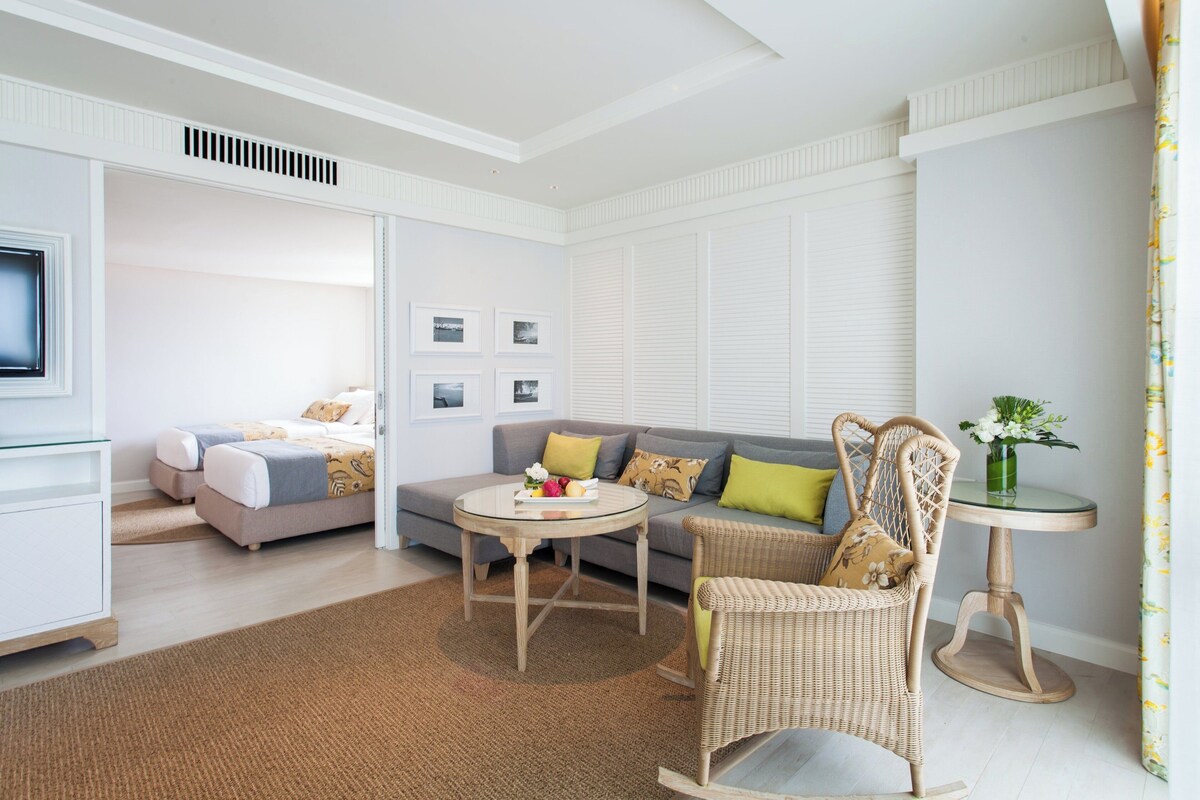 Una habitación de hotel moderna con sofá, una mesa redonda, una silla de mimbre, cama y televisor.