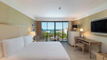 Habitación de hotel con una cama grande, un escritorio, una silla, un televisor y vista al océano.