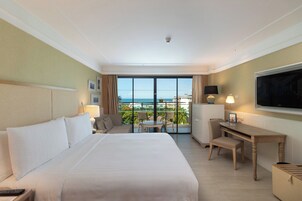 Habitación de hotel con una cama grande, un escritorio, una silla, un televisor y vista al océano.