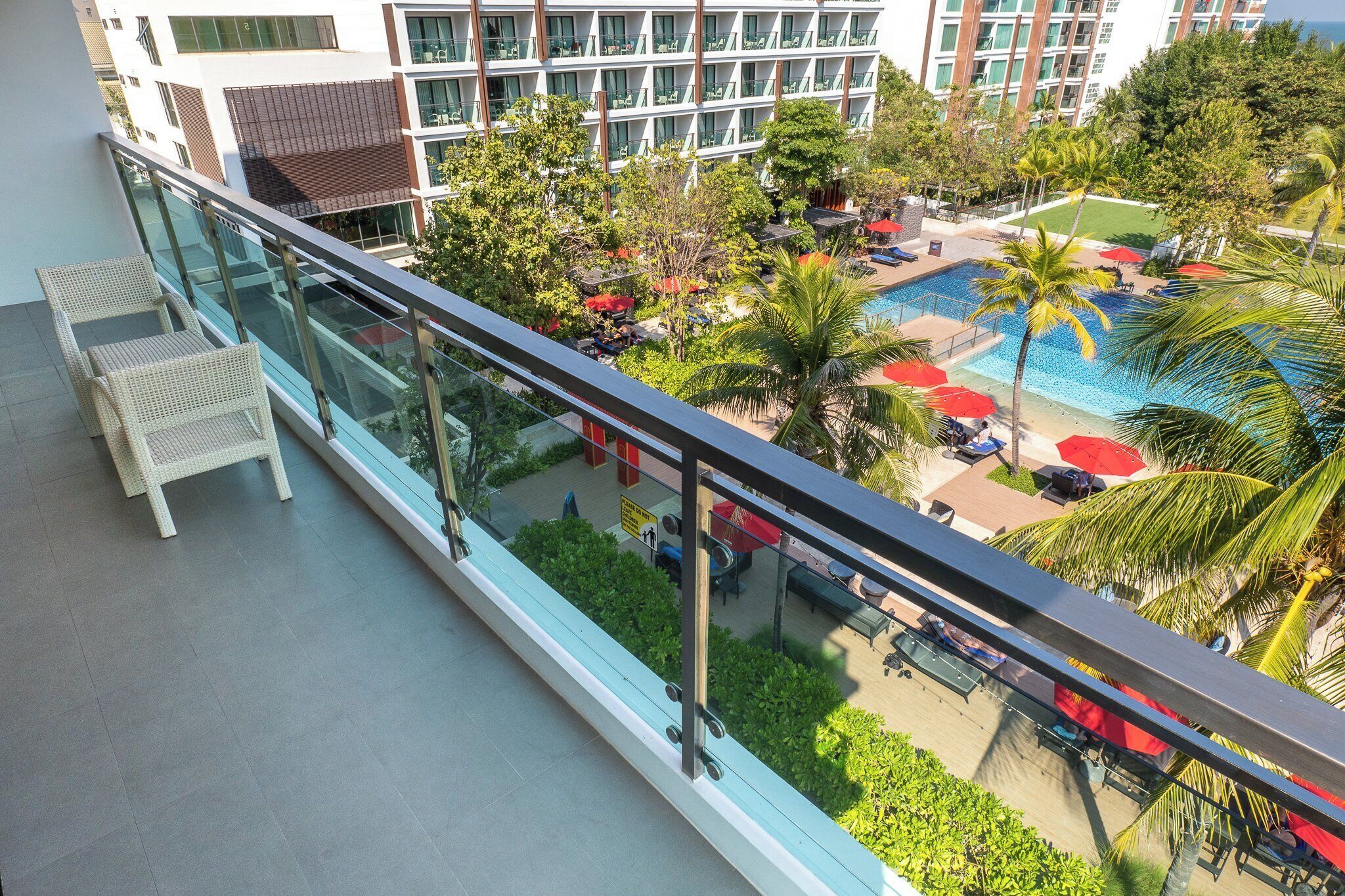 A balcony with a glass railing overlooking a pool area with lounge chairs and umbrellas.
