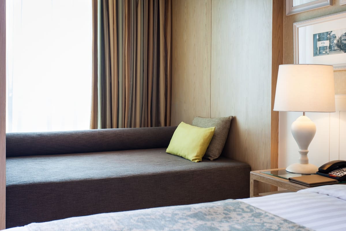 Habitación de hotel con sofá, mesita de noche con lámpara, teléfono y un cuadro en la pared.