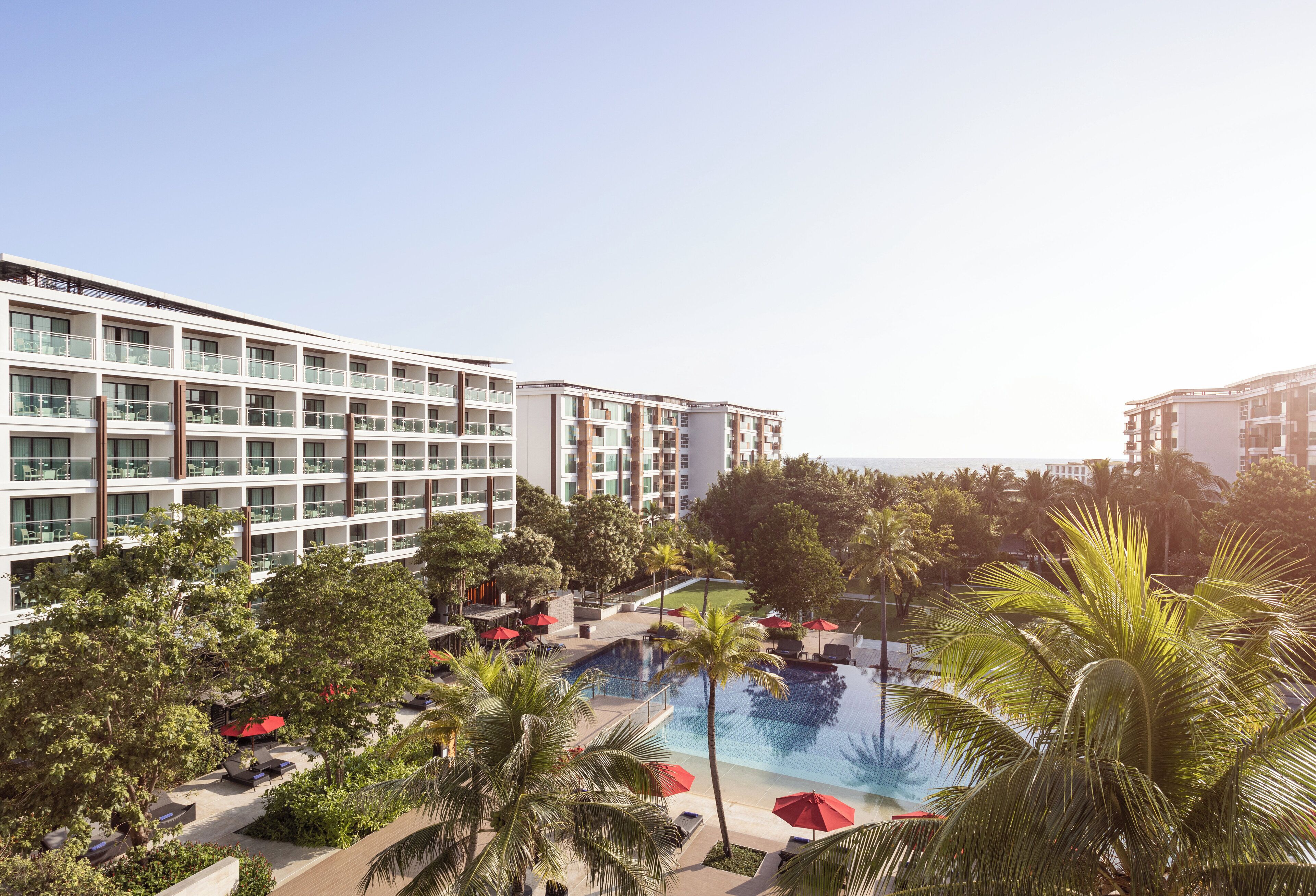 A hotel with a pool area surrounded by palm trees and lounge chairs.