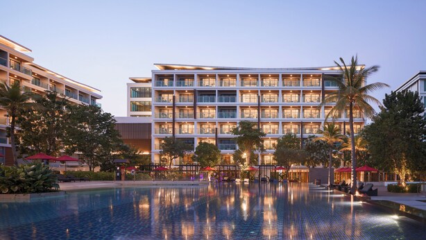 Un hotel moderno con varios pisos, piscina y zonas de estar al aire libre.