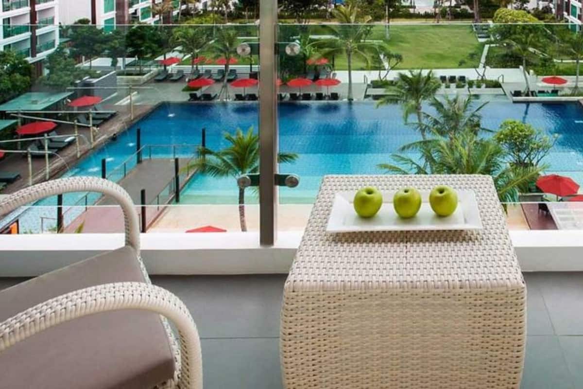 Un balcón con sillas de mimbre, una mesa con manzanas y vista a una piscina y zona de descanso.