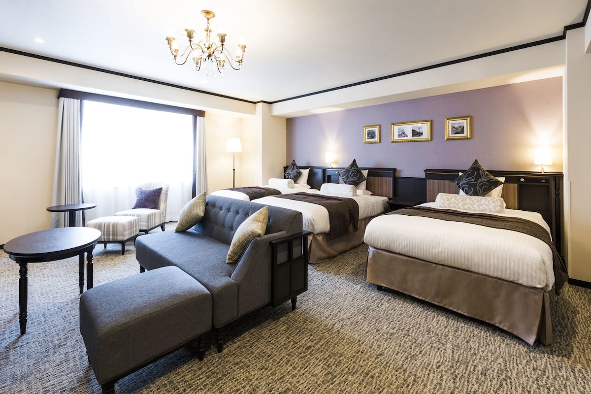 A hotel room with a large bed, a sofa, a small table, and a chandelier.
