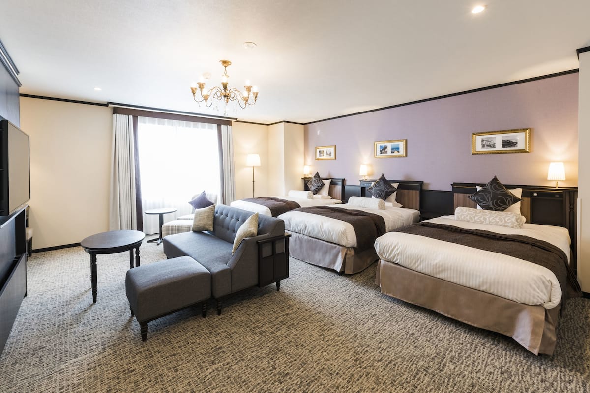 A hotel room with a large bed, two smaller beds, a sofa, a TV, and a chandelier.