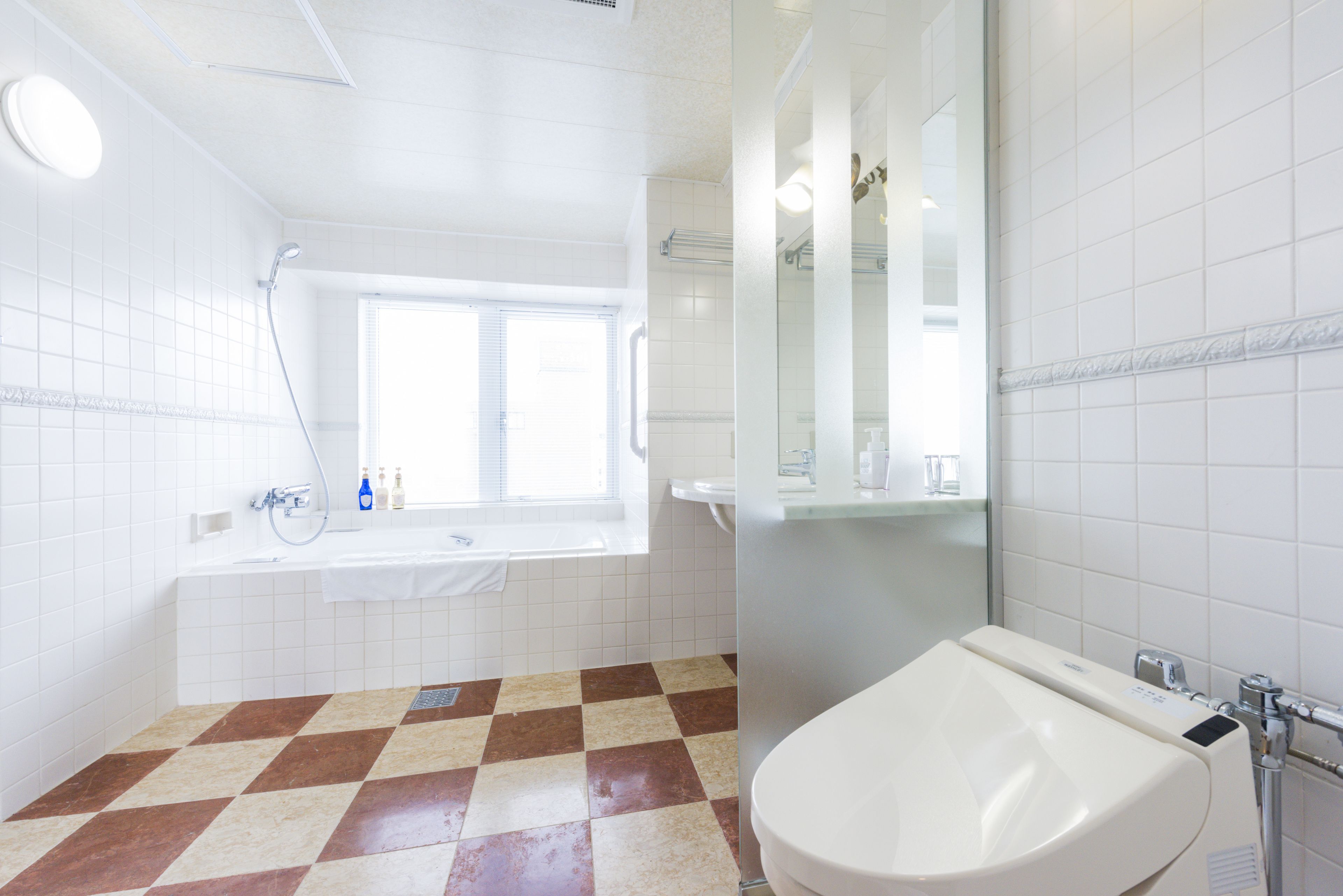 Un baño con piso a cuadros, un lavamanos blanco, una bañera y un espejo grande.