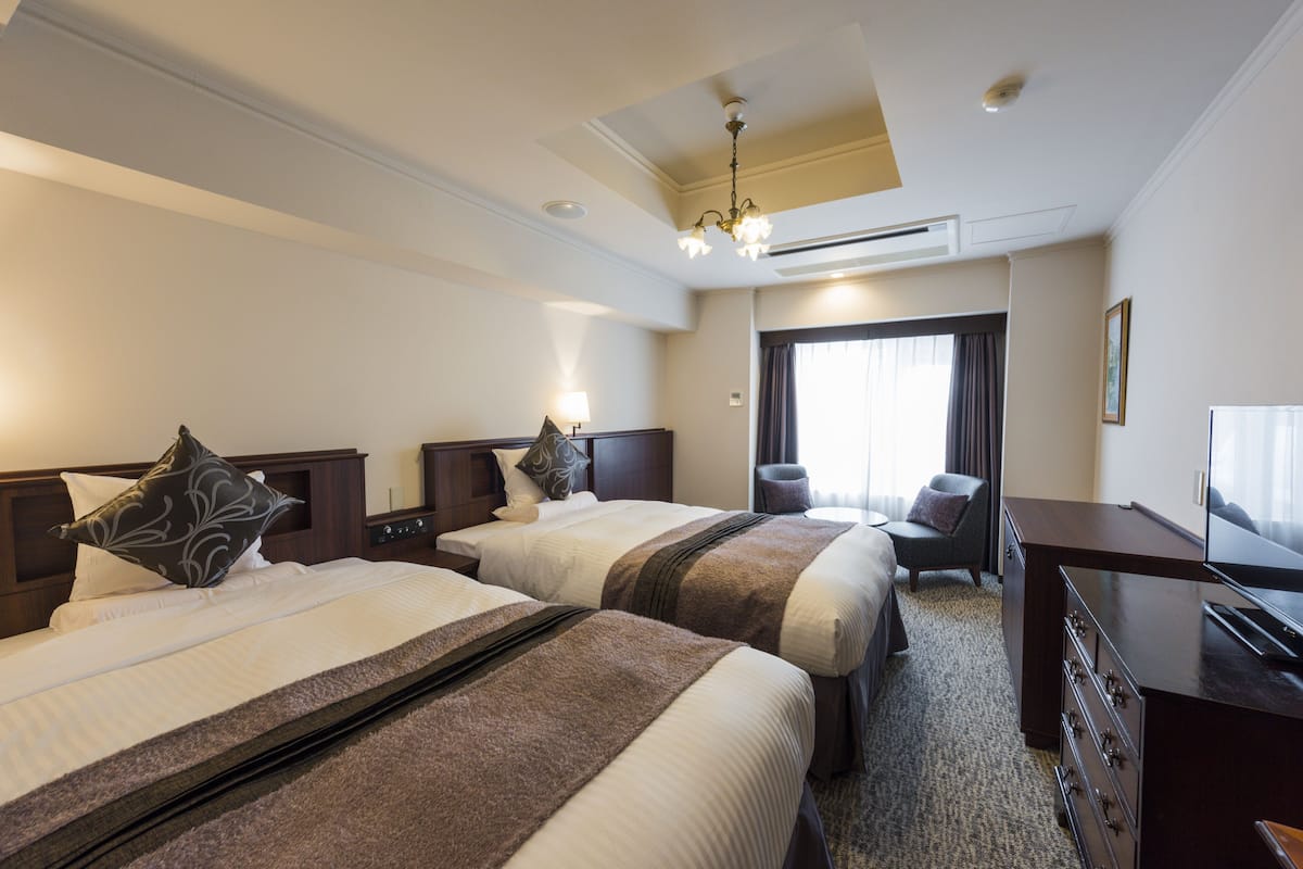A hotel room with two beds, a desk, a chair, and a television.