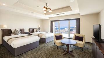 A hotel room with two beds, a TV, a small table, and a view of the ocean.