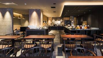 A modern restaurant with multiple dining tables and chairs, a central bar area with a variety of food and drink options, and a kitchen in the background.