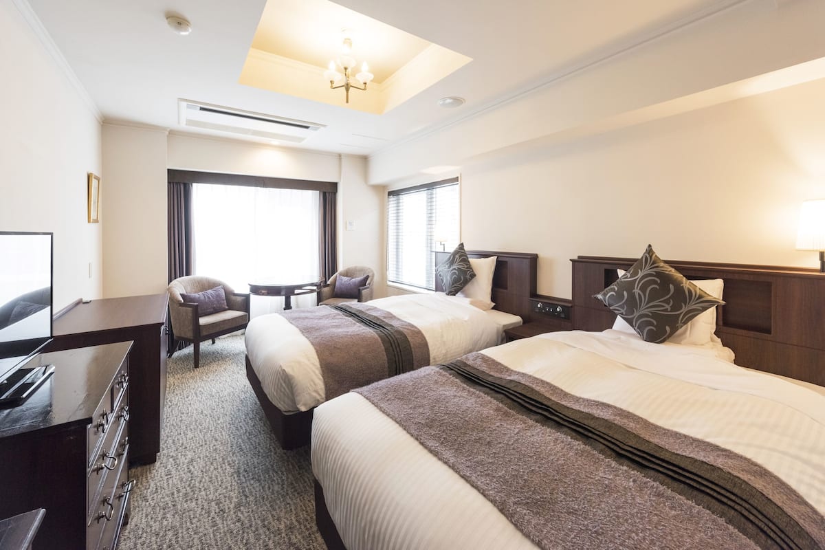 A hotel room with two beds, a desk, a chair, and a TV.