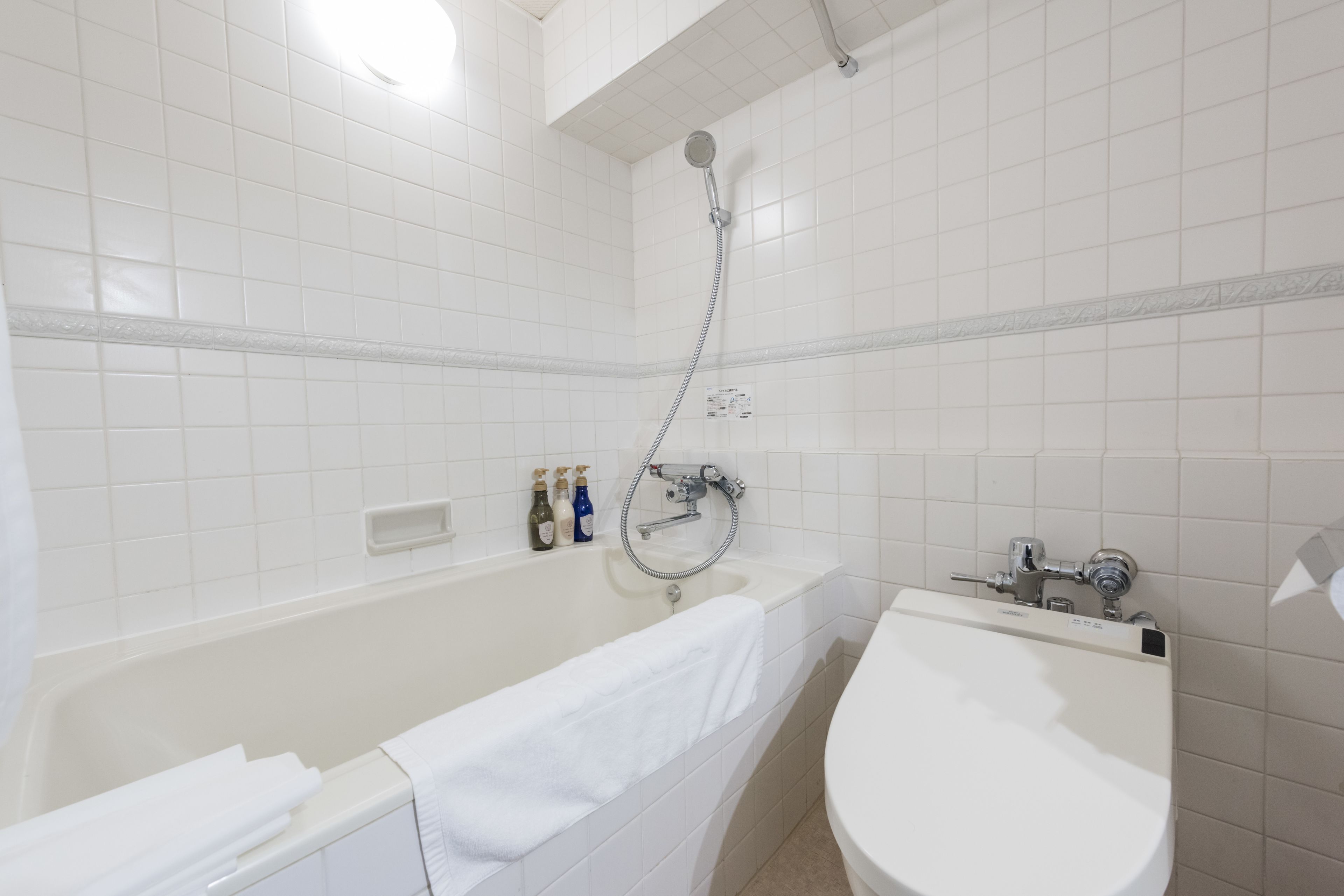 A bathroom with a bathtub, a sink, and a shower. There are bottles of toiletries on the wall.