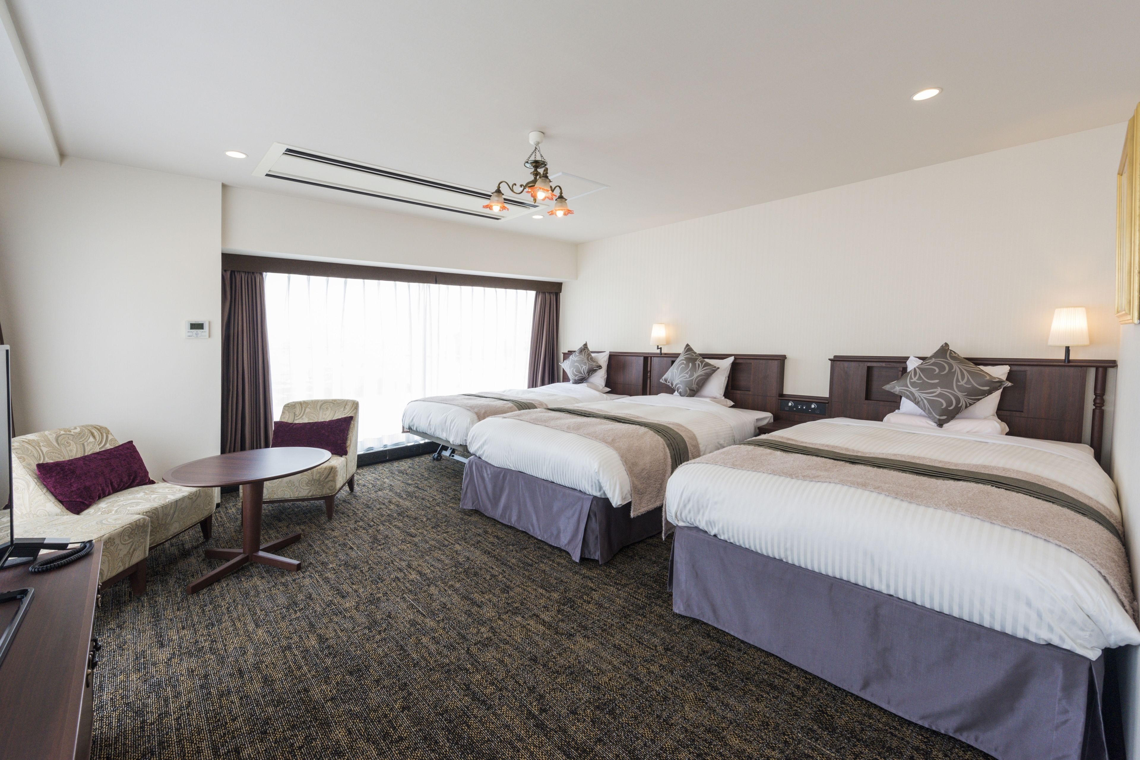 A hotel room with two beds, a sofa, a small table, and a window with curtains.