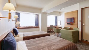 Una habitación de hotel con dos camas, un escritorio, una silla, un televisor y una ventana con cortinas.