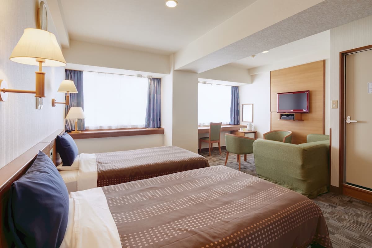 A hotel room with two beds, a desk, a chair, a television, and a window with curtains.