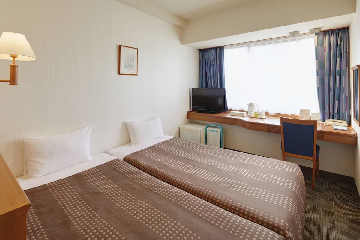 Une chambre d’hôtel avec deux lits, un bureau, une télévision et une fenêtre avec des rideaux.