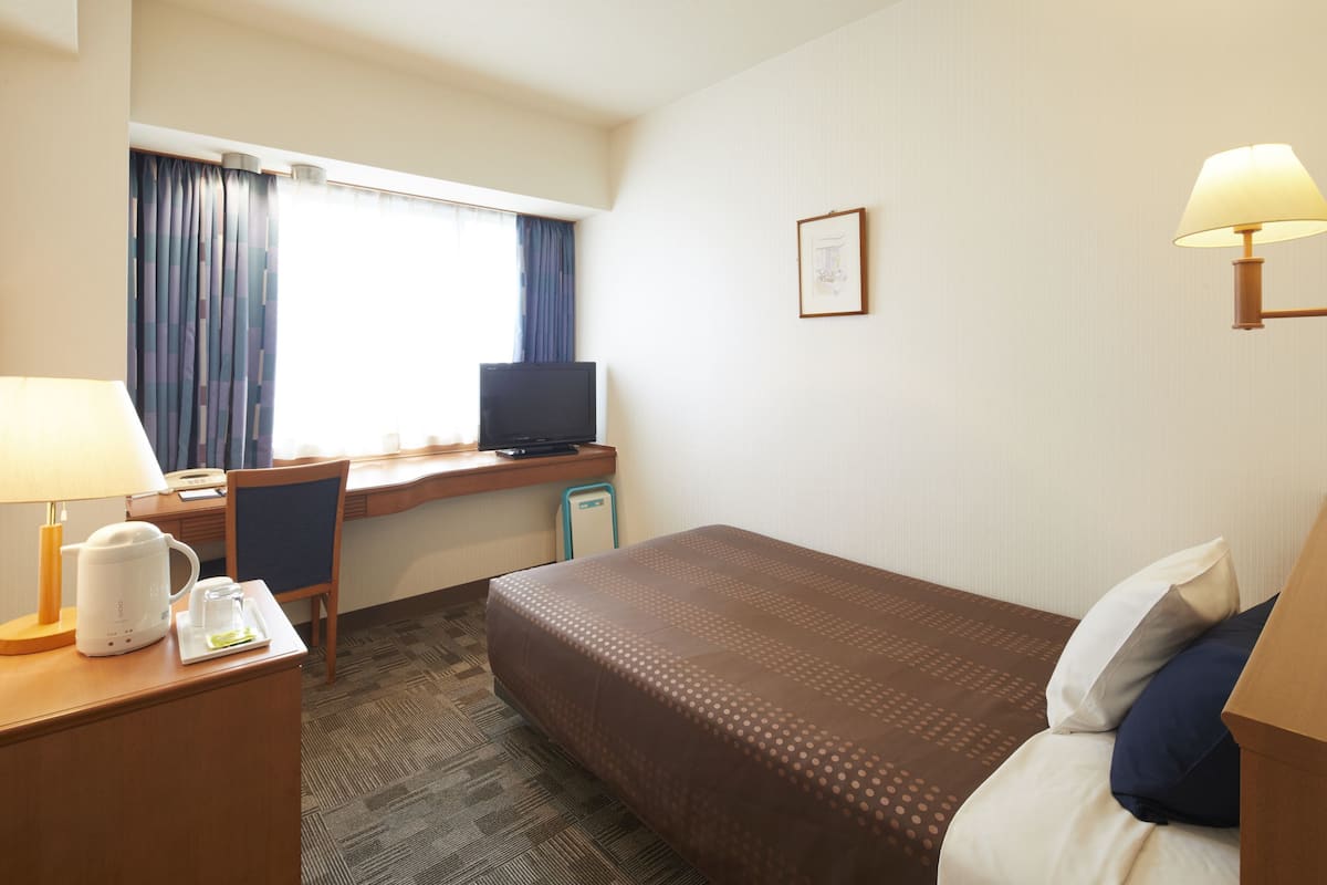 Une chambre d’hôtel équipée d’un lit, d’un bureau, d’une chaise, d’une télévision et d’une fenêtre avec des rideaux.
