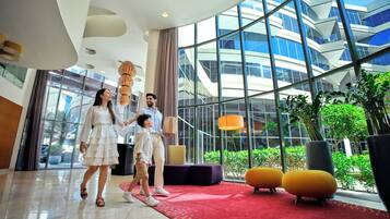 A modern hotel lobby with a red carpet, large windows, and indoor plants.