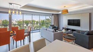 A modern living room with a large TV, comfortable seating, a dining area, and a balcony with a city view.