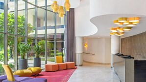 A modern lobby with a reception desk, purple and yellow seating, large windows, and a red carpet.