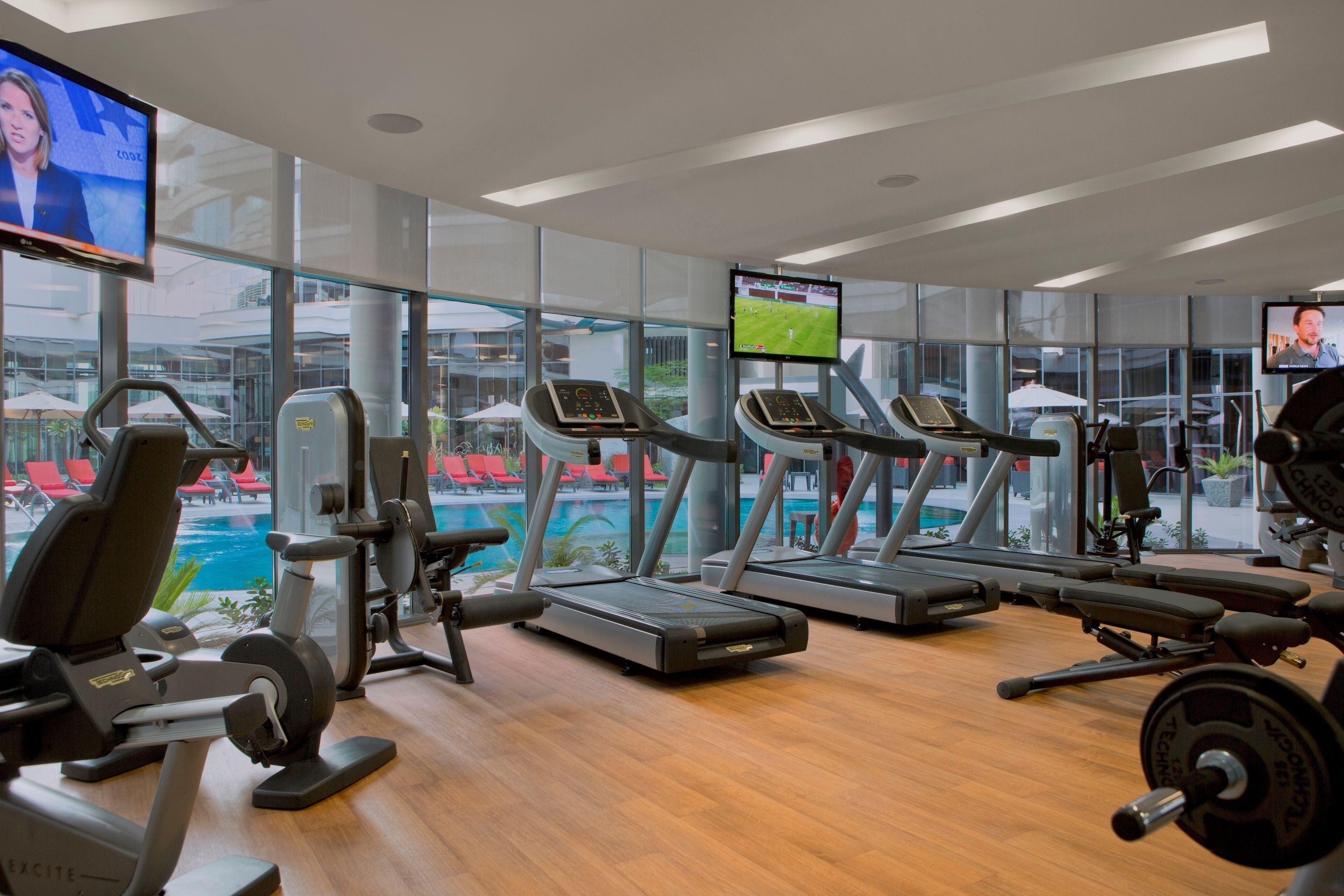 Une salle de sport moderne dotée de tapis de course, d’appareils de musculation et offrant une vue sur la piscine.