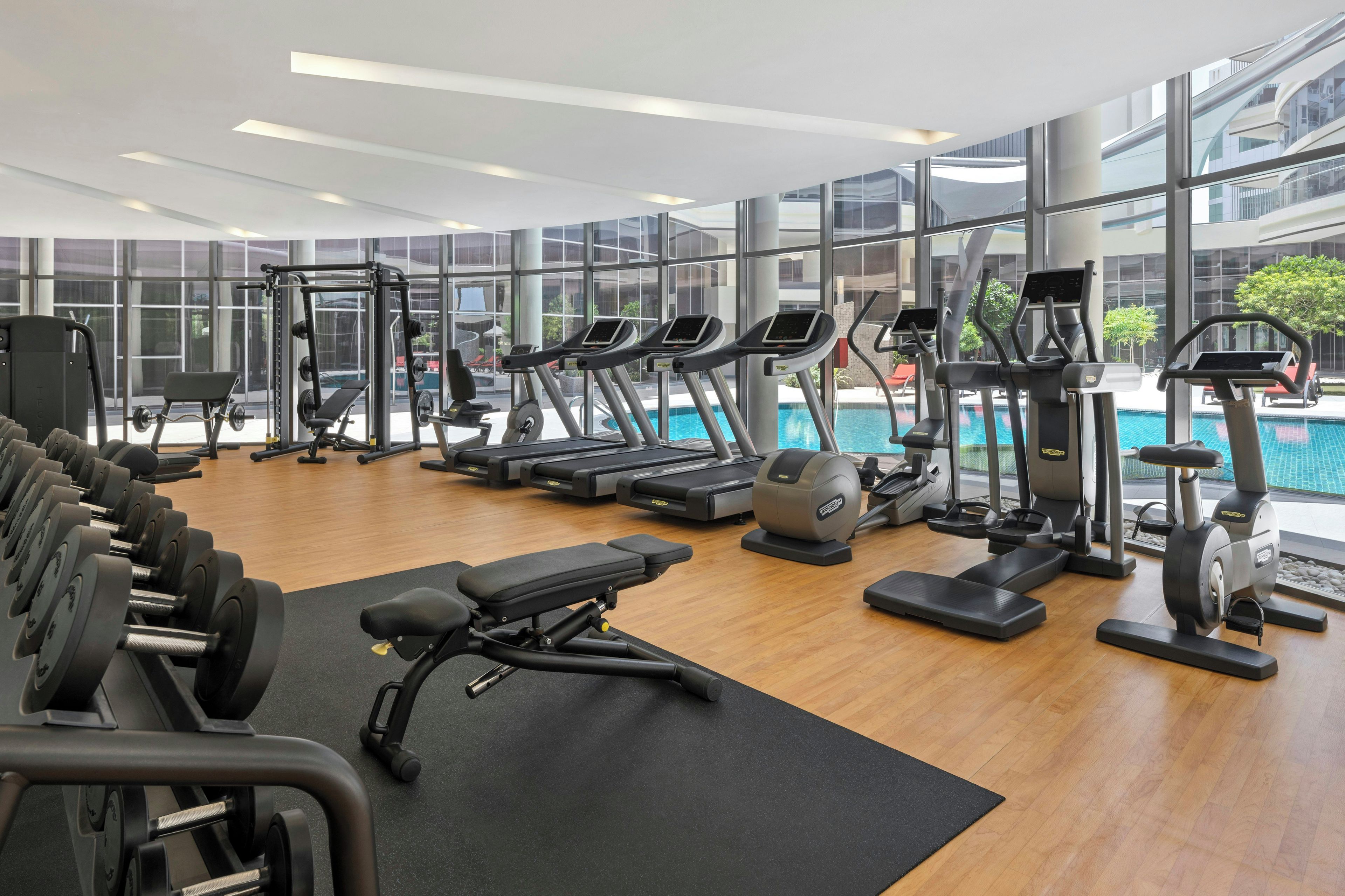 Un gimnasio moderno con diversos equipos de ejercicio, piso de madera y amplios ventanales con vistas al exterior.