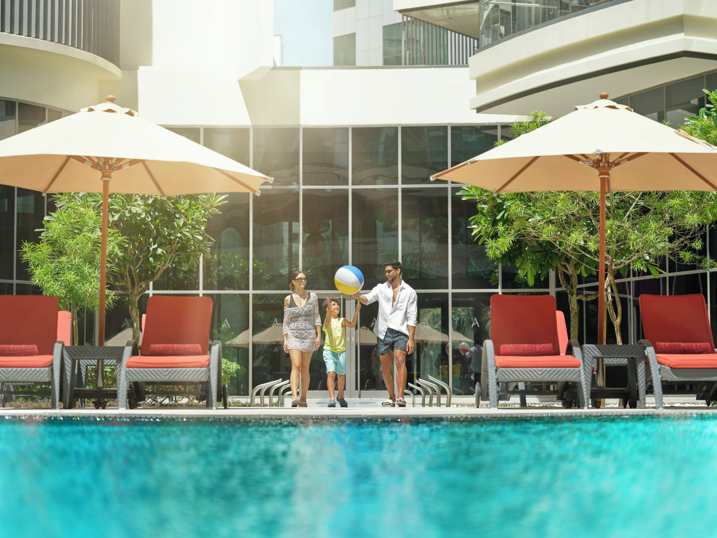 A swimming pool area with lounge chairs and umbrellas, surrounded by a modern building with large windows.