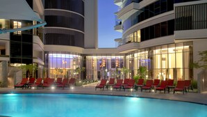 A modern hotel with a pool area, red lounge chairs, and a well-lit interior.