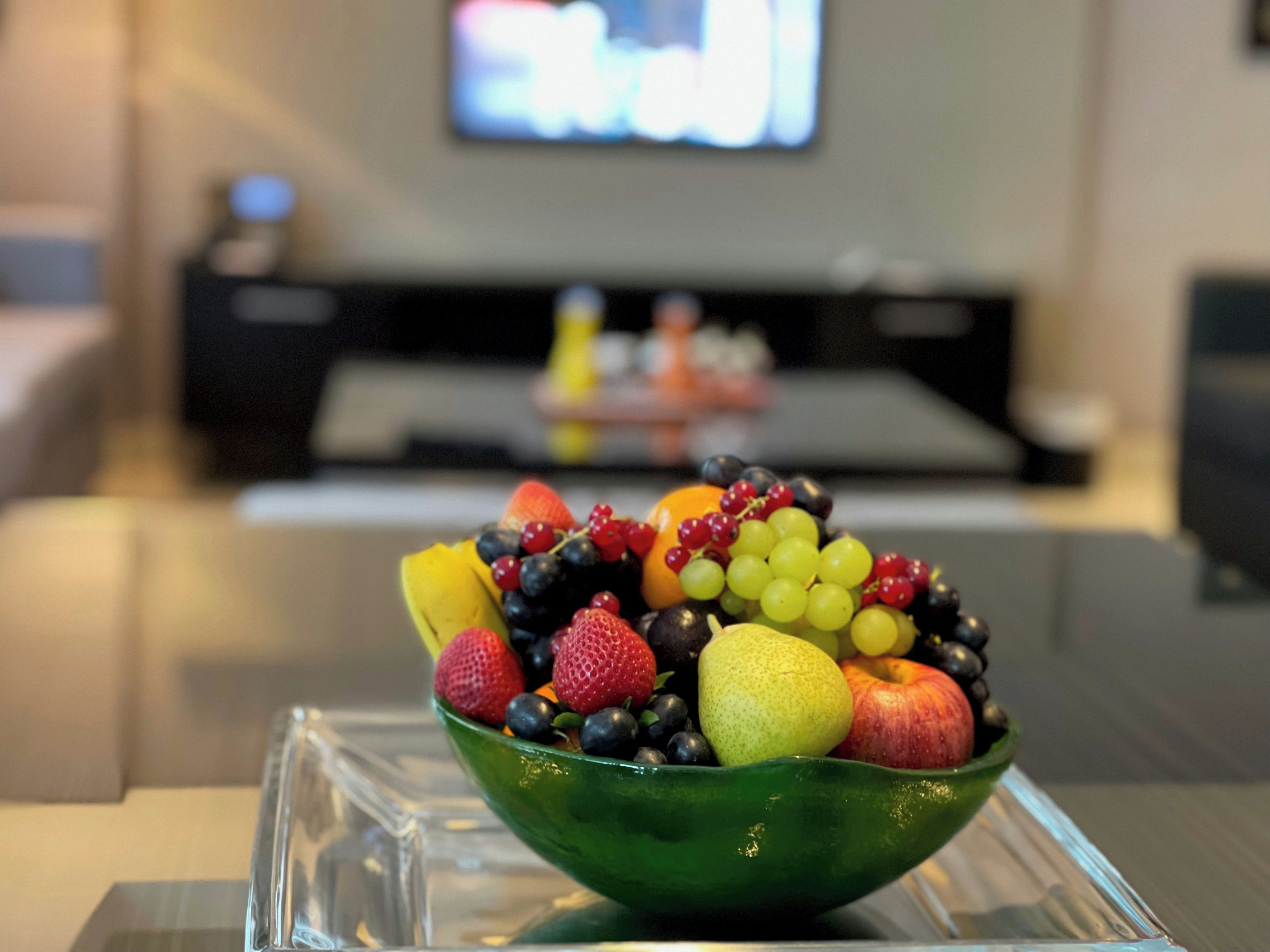 A bowl of assorted fruits on a clear glass stand.