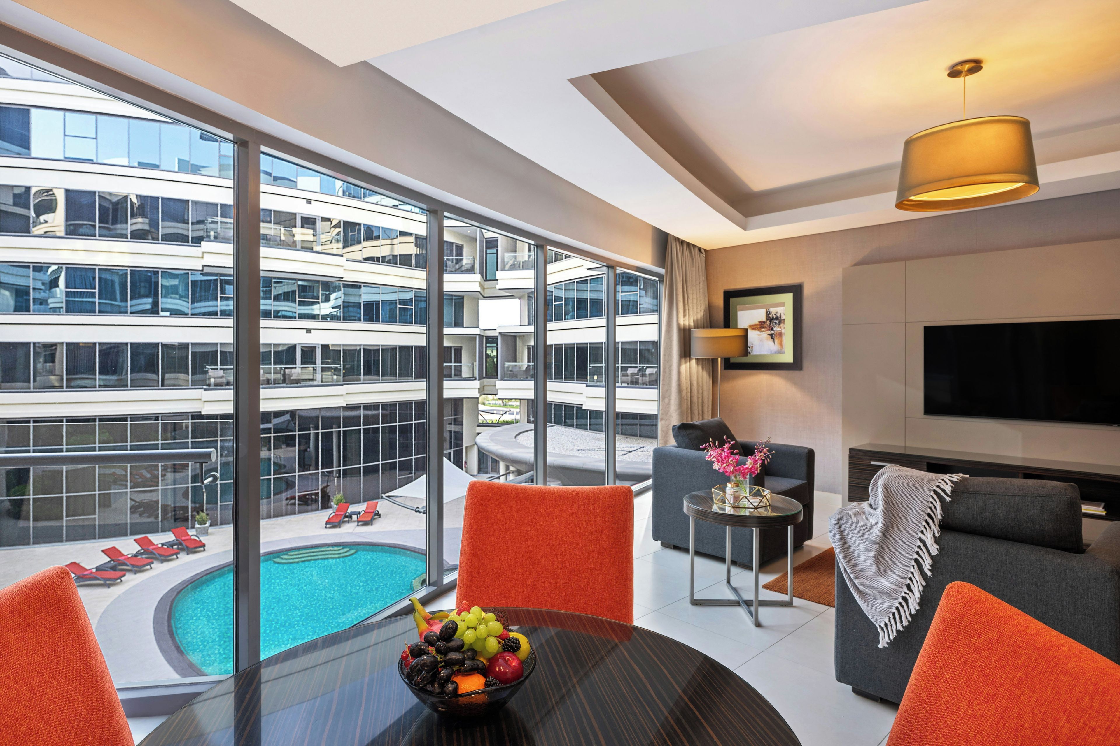 A modern hotel room with a balcony, a pool, and a dining area with fruit.