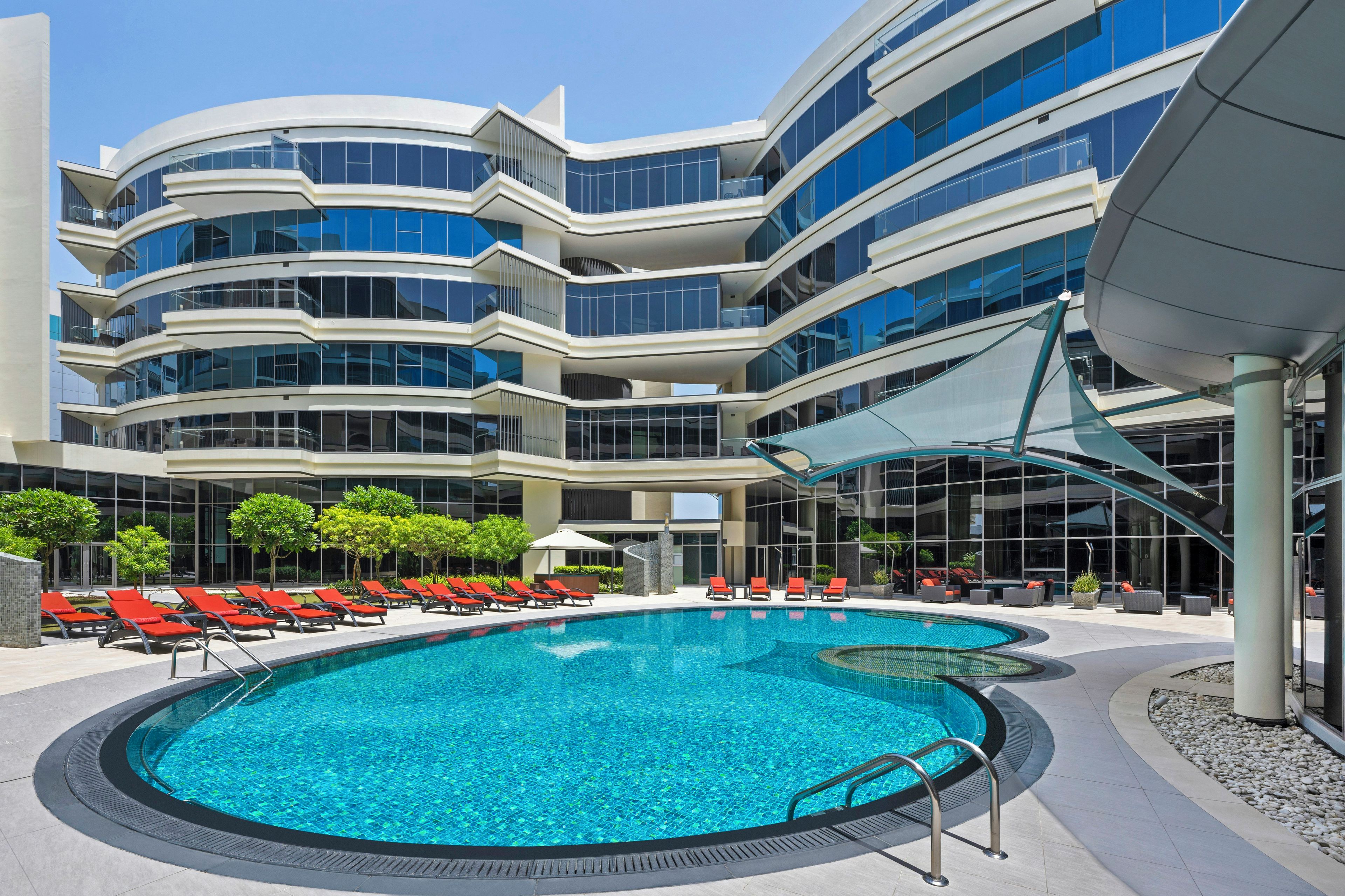 Un hotel moderno con piscina, varios balcones y zonas de estar al aire libre.