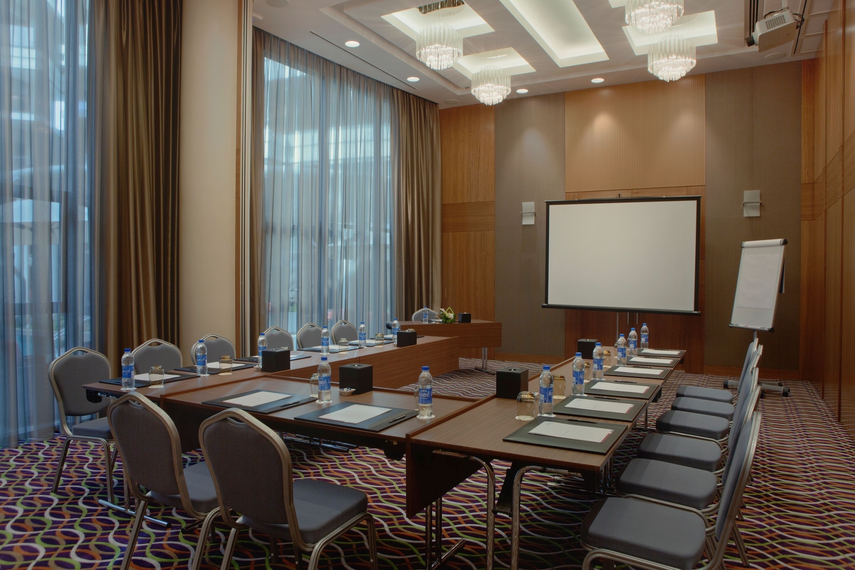 Un salón de conferencias con una larga mesa, sillas, una pantalla de proyector y una pizarra.
