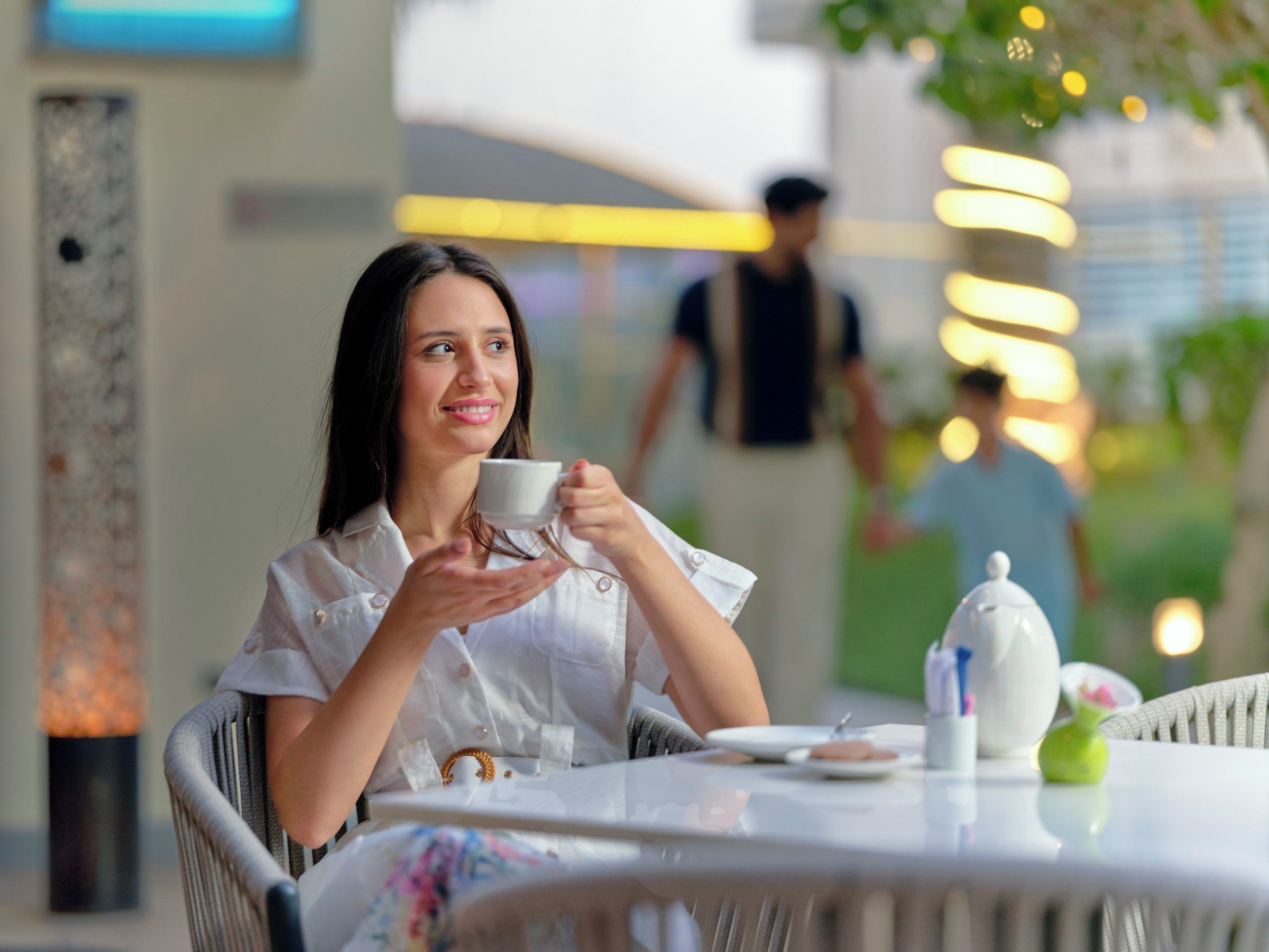A person seated at a table with a cup, a teapot, and a plate.
