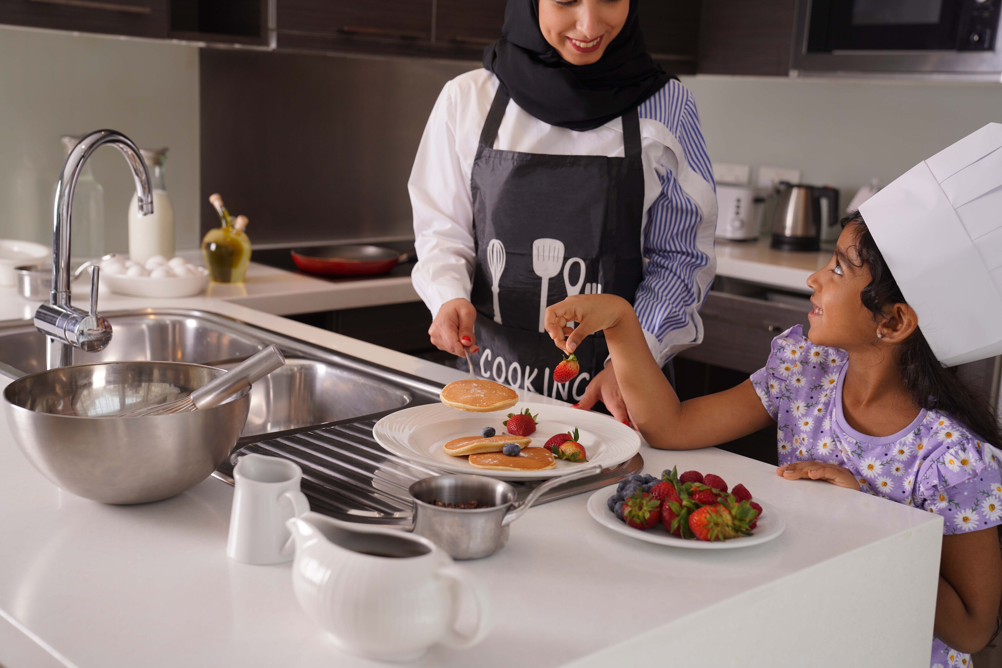 Una cocina moderna con electrodomésticos de acero inoxidable, una encimera blanca y una persona preparando panqueques.